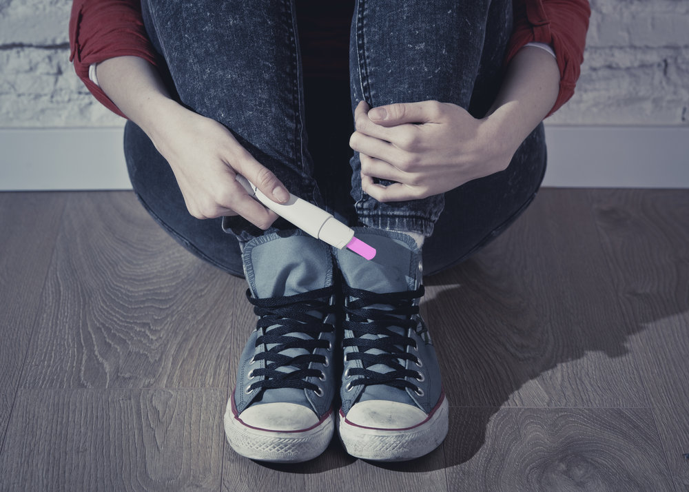 conceptual image hand of pregnant teenager girl or young desperate woman holding positive pink pregnancy test sitting on home floor in unwanted baby and unexpected motherhood concept